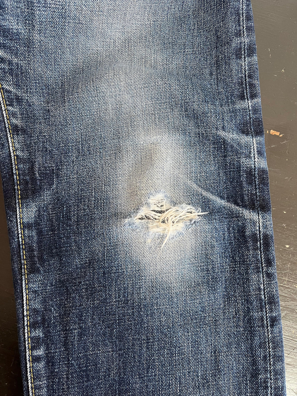 Jeans knee repaired with colour-matched stitching
